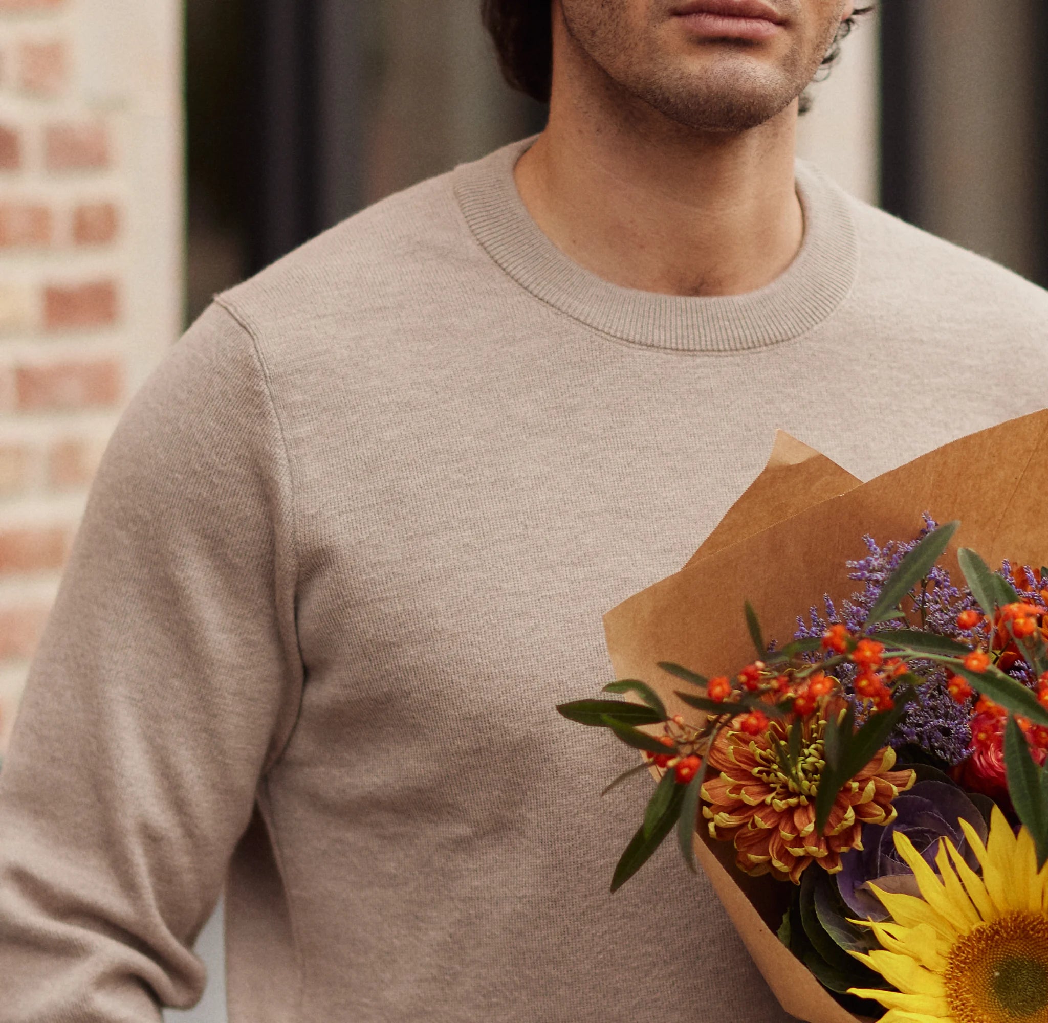 Man wearing a beige sweater holding a bouquet of flowers against a blurred background