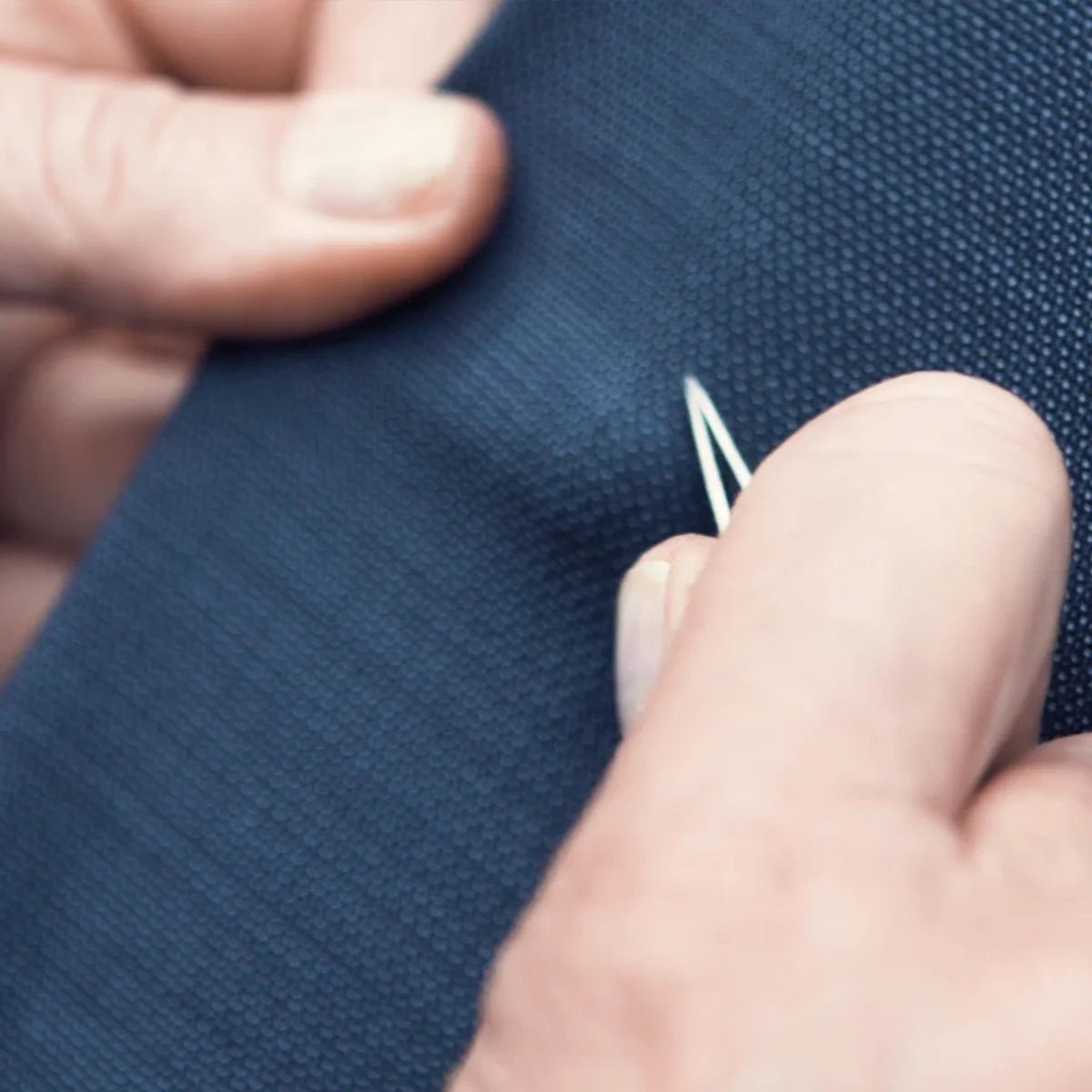 Close-up of hands quality checking on blue fabric with a needle.
