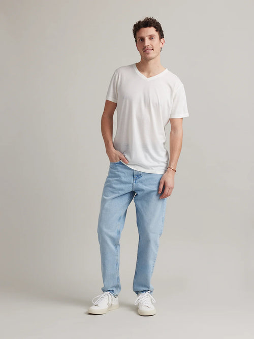Male model wears a white merino wool T-shirt with V neck on a light blue denim jeans.