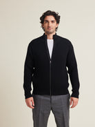 Man wears a full zip merino wool cardigan in black color and sidepockets from Wolk