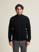 men wears a 100% merino wool knit vest in half cardigan knit with high collar in black color made in heavy weight superfine responsible merino wool