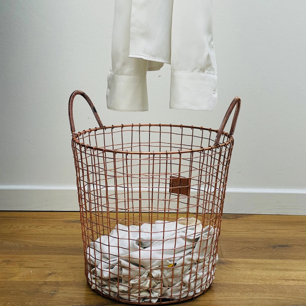 Wire laundry basket filled with white clothes on a wooden floor.