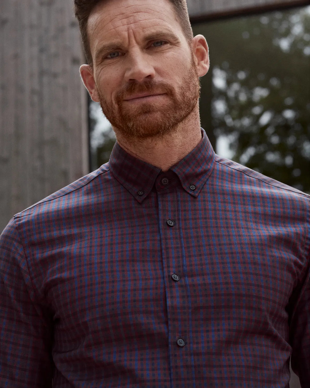 man wearing a burgundy checkered merino button-down shirt with a blurred backround showing reflection in a window