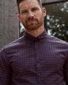 man wearing a burgundy checkered merino button-down shirt with a blurred backround showing reflection in a window