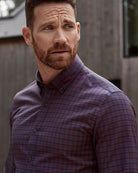 man wearing a burgundy checkered merino button-down shirt outdoors with a house in the background 