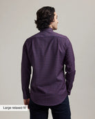 back view of a man wearing a burgundy checkered merino button-down shirt tucked in dark denim with a beige background