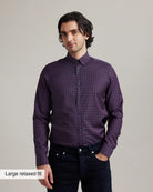 man wearing a burgundy checkered merino button-down shirt tucked in dark denim with a beige background