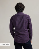back view of a man wearing a burgundy checkered merino button-down shirt untucked on dark denim with a beige background
