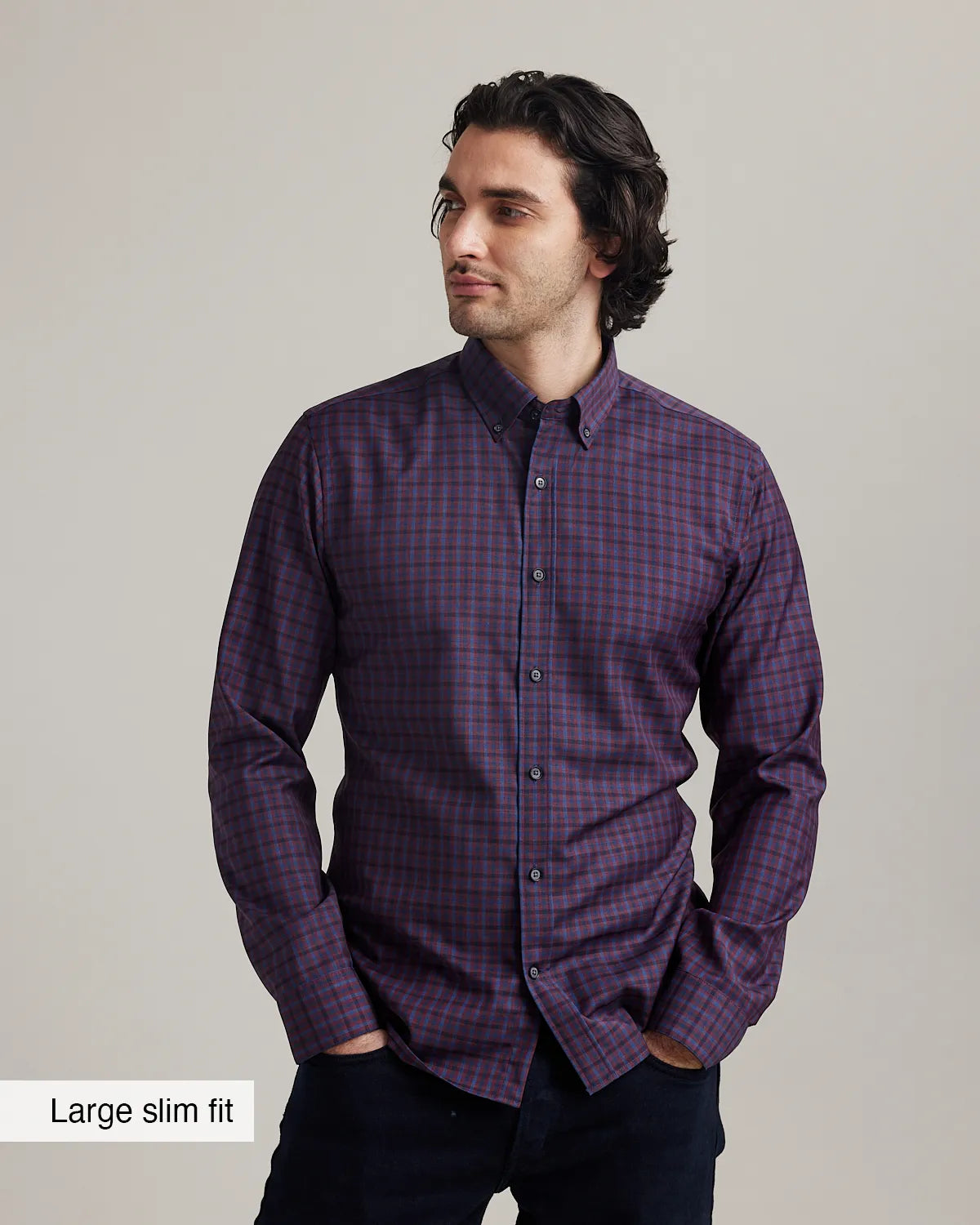 man wearing a burgundy checkered merino button-down shirt untucked on dark denim with a beige background