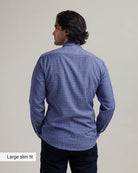 back view of a man wearing a blue/red checkered merino wool button down shirt in slip fit on a grey background