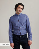 Man wearing a blue/red checkered merino wool button down shirt tucked in dark navy jeans with a gray background
