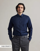 Man wearing a navy blue merinowool dress shirt in relaxed fit and gray pants on a plain background