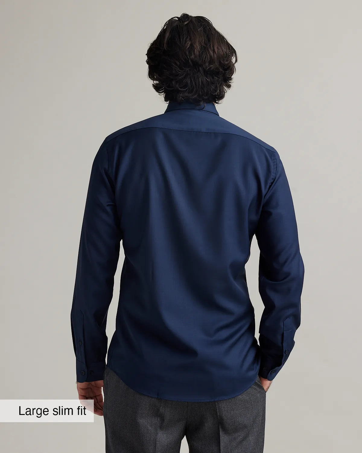 back view of a man wearing a navy blue merinowool dress shirt in slim fit on a plain background