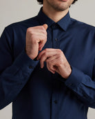 Man adjusting cuff on a navy blue merino shirt against a neutral background