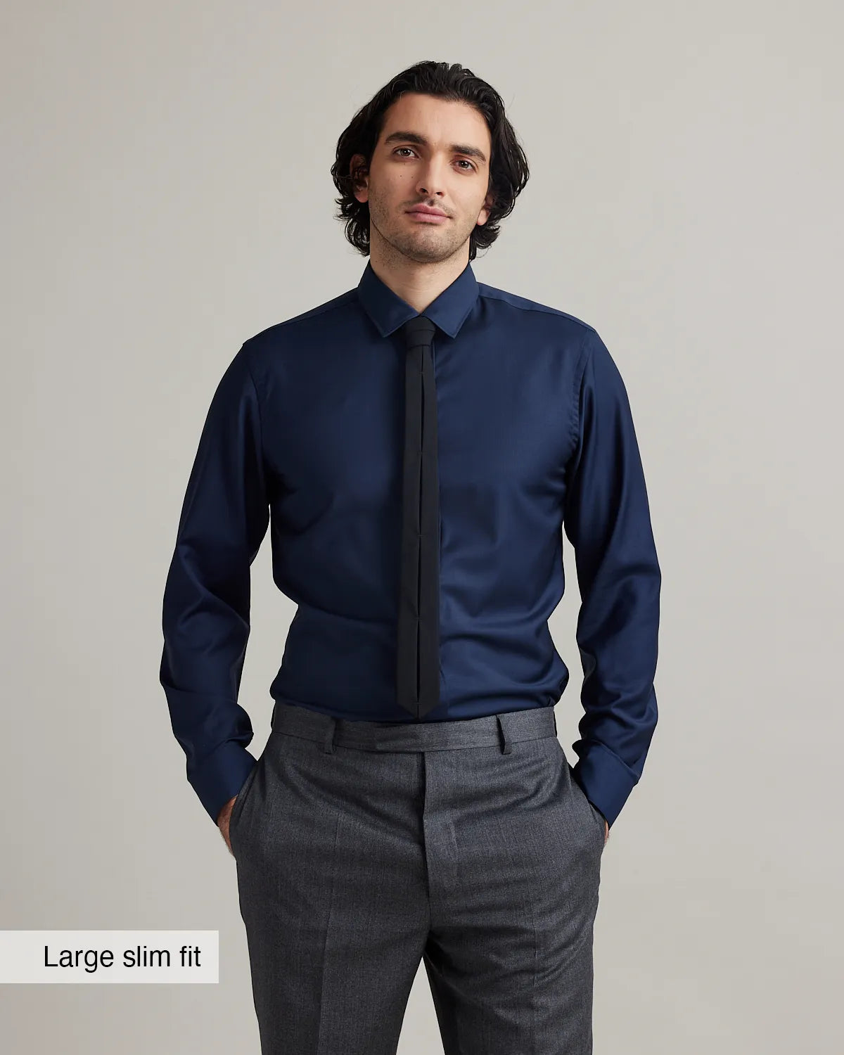 Man wearing a navy merinowool dress shirt in slim fit with a black tie and gray pants against a plain background