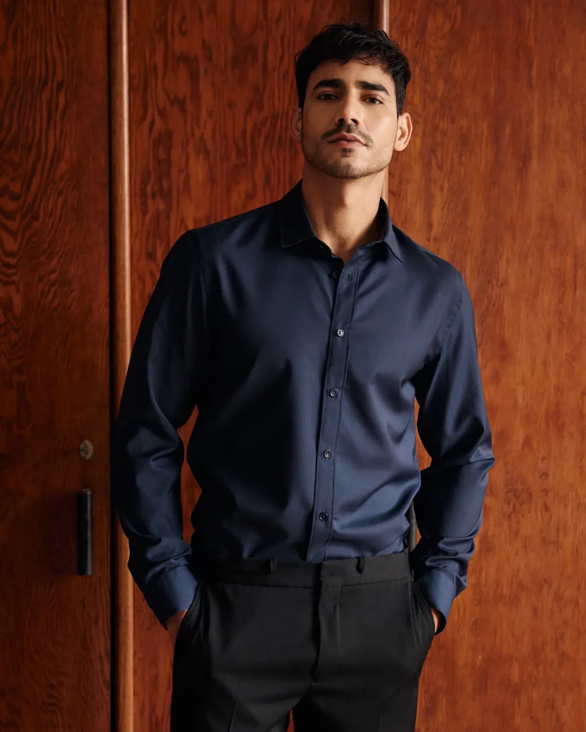 Man wearing a navy blue merinowool dress shirt in slim fit and black pants against a wooden door background