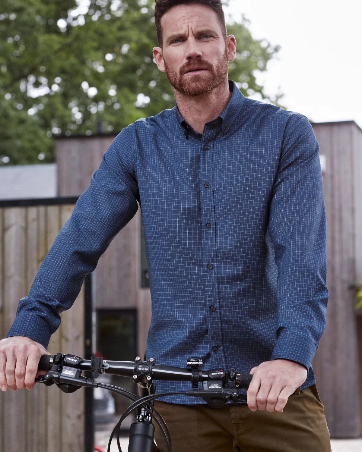 Man wearing a blue checkered merino shirt from Wolk standing next to a bicycle outdoors.