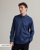 Man wearing a navy blue merino shirt with graph check pattern and button down collar against a gray background