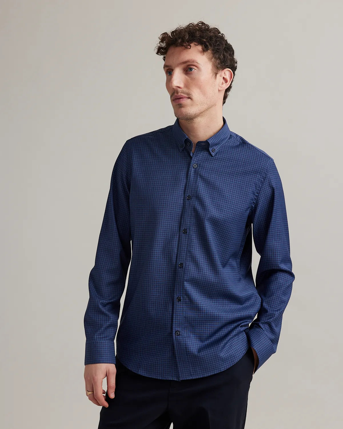 Man wearing a navy blue merino shirt with graph check pattern and button down collar against a plain background