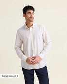 Man wearing a white merinowool dress shirt with a relaxed fit untucked with navy trousers on a beige background