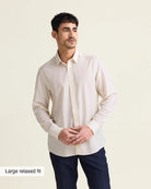 Man wearing a white merinowool dress shirt with a relaxed fit untucked with navy trousers on a beige background