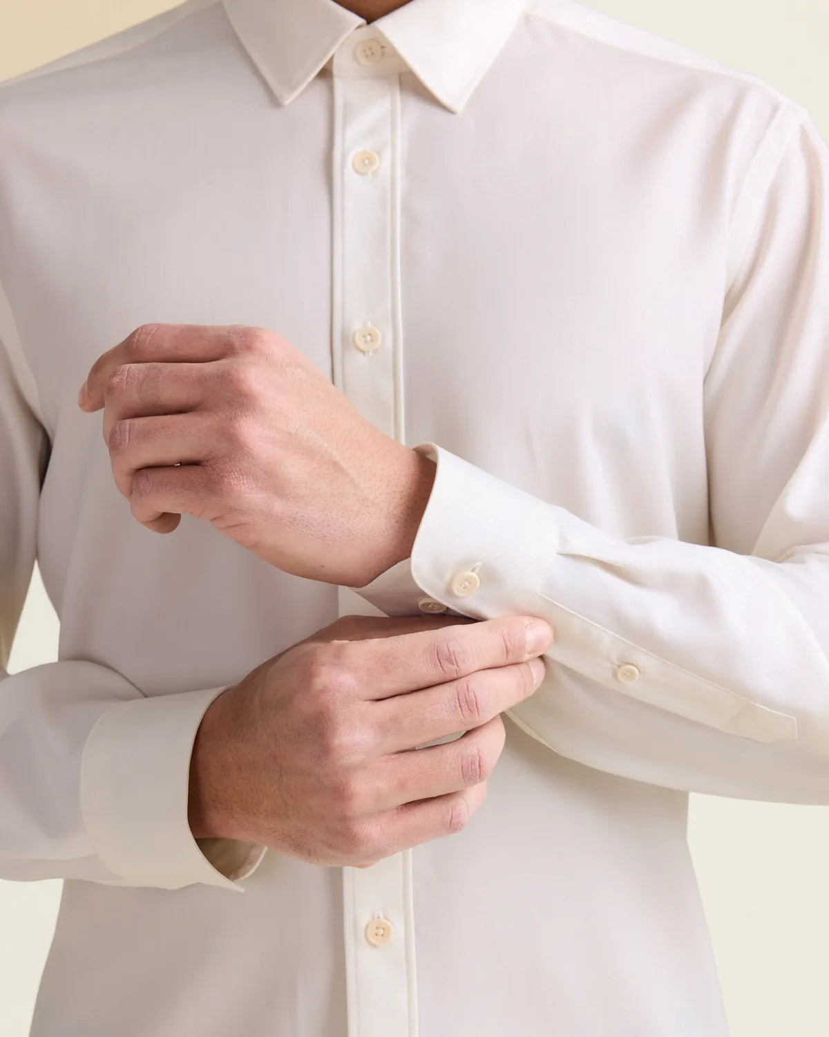 Person adjusting the cuff of a white merino wool dress shirt against a light background