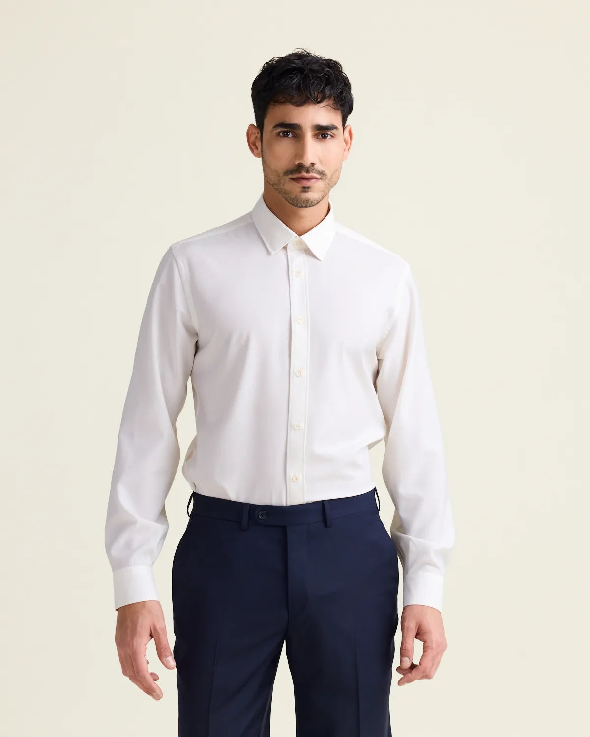 Man wearing a white merinowool dress shirt from Wolk in slim fit with navy trousers on a beige background