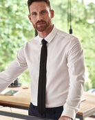 Man wearing a white merino wool dress shirt from the brand Wolk and black tie indoors with a blurred green outdoor background
