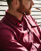 Man wearing a red merino button-down shirt sitting on a wooden bench with sunglasses