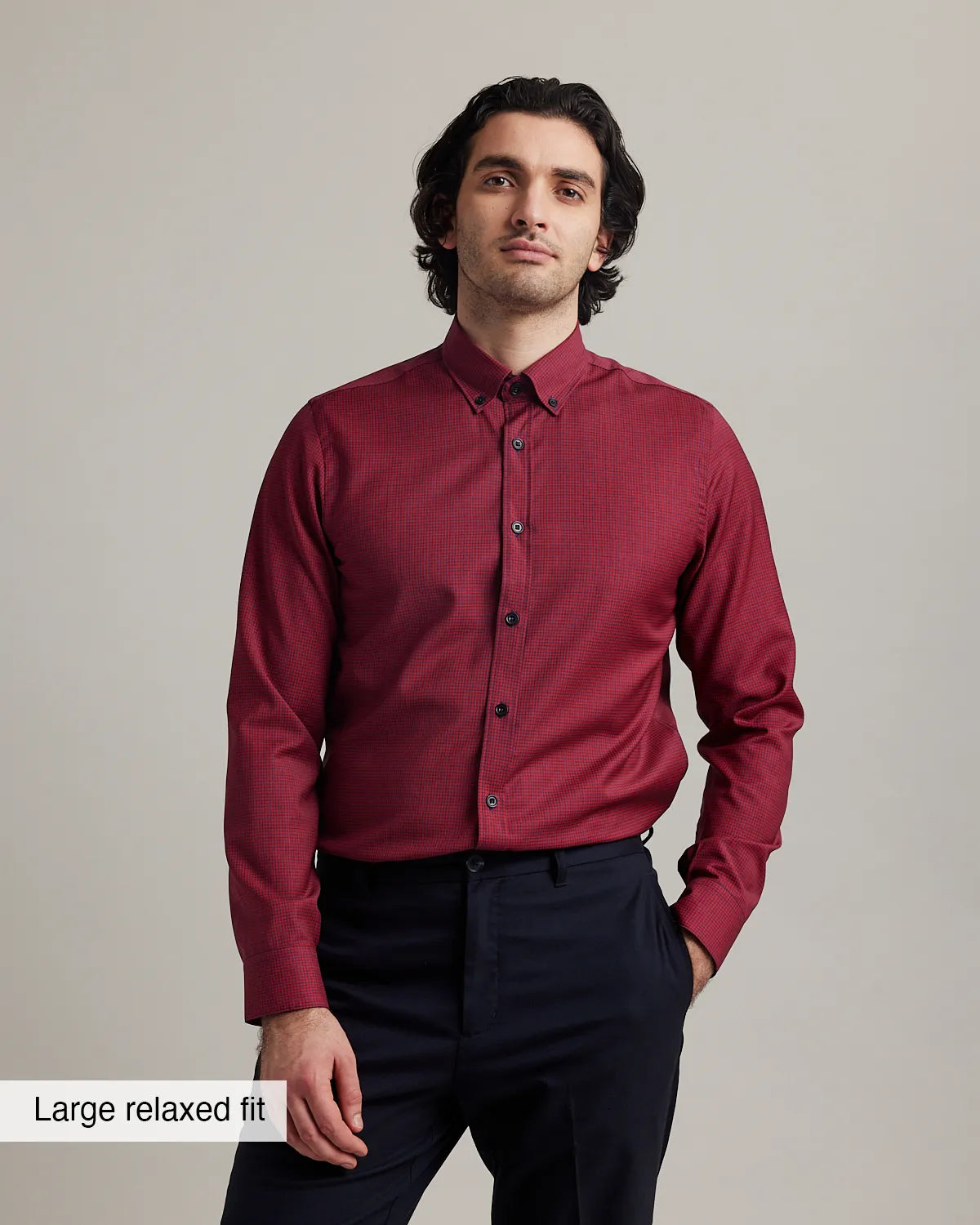 Man wearing a red checkered merinowool button dosn shirt in relaxed fit on navy trousers on a gray background
