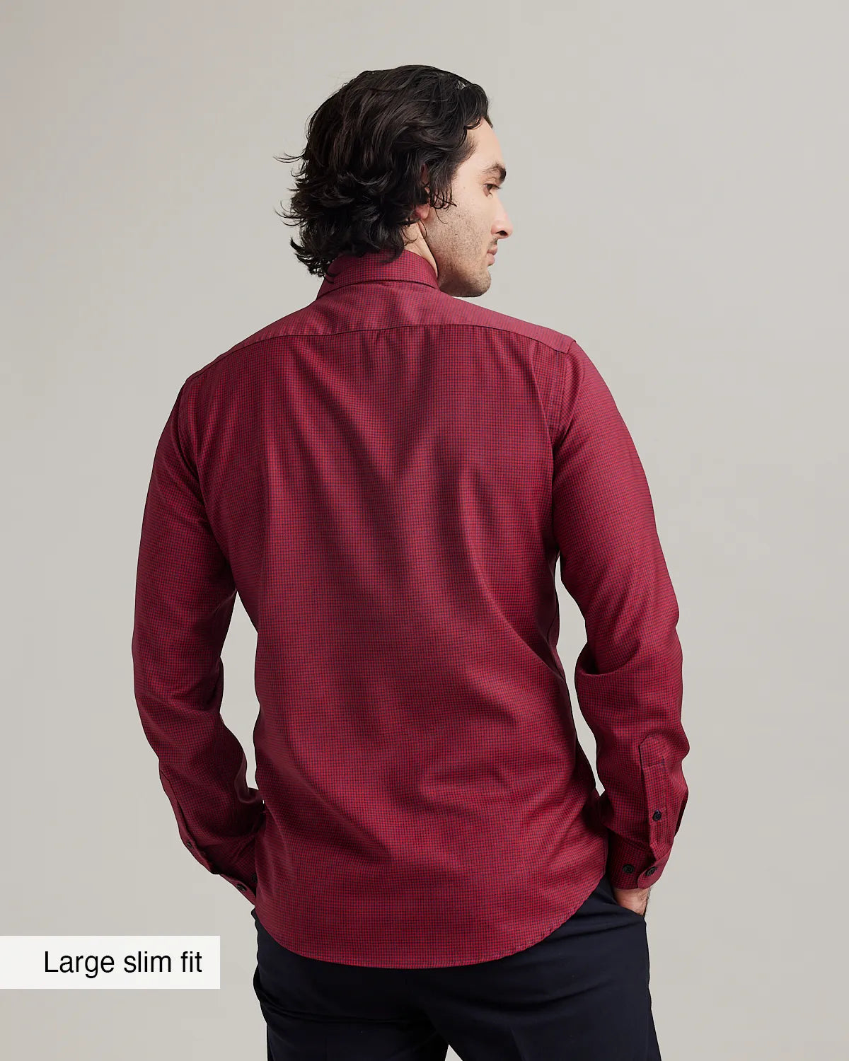 back view of a male model wearing a red merino button-down shirt with long sleeves on navy trousers against a gray background