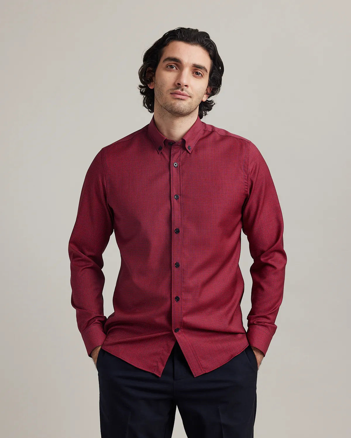 Man wearing a red merino button-down shirt on navy trousers against a plain background
