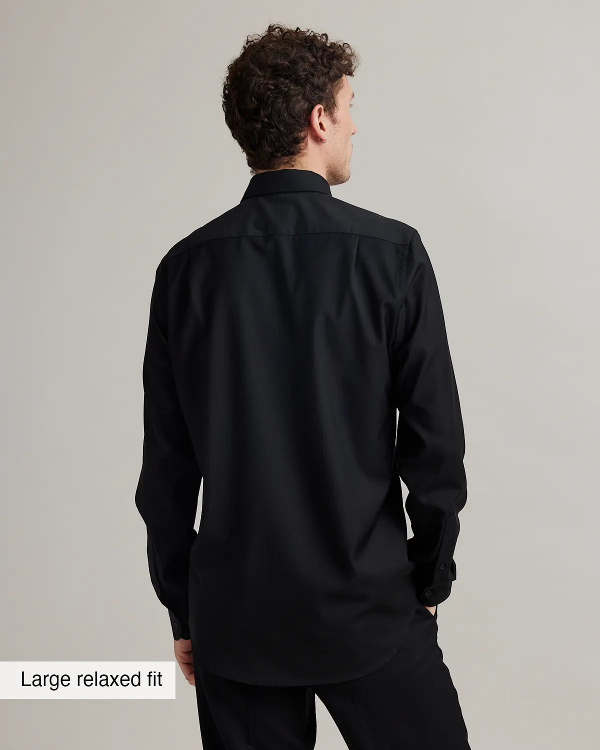Man wearing a black merinowool shirt with a large relaxed fit label on a gray background