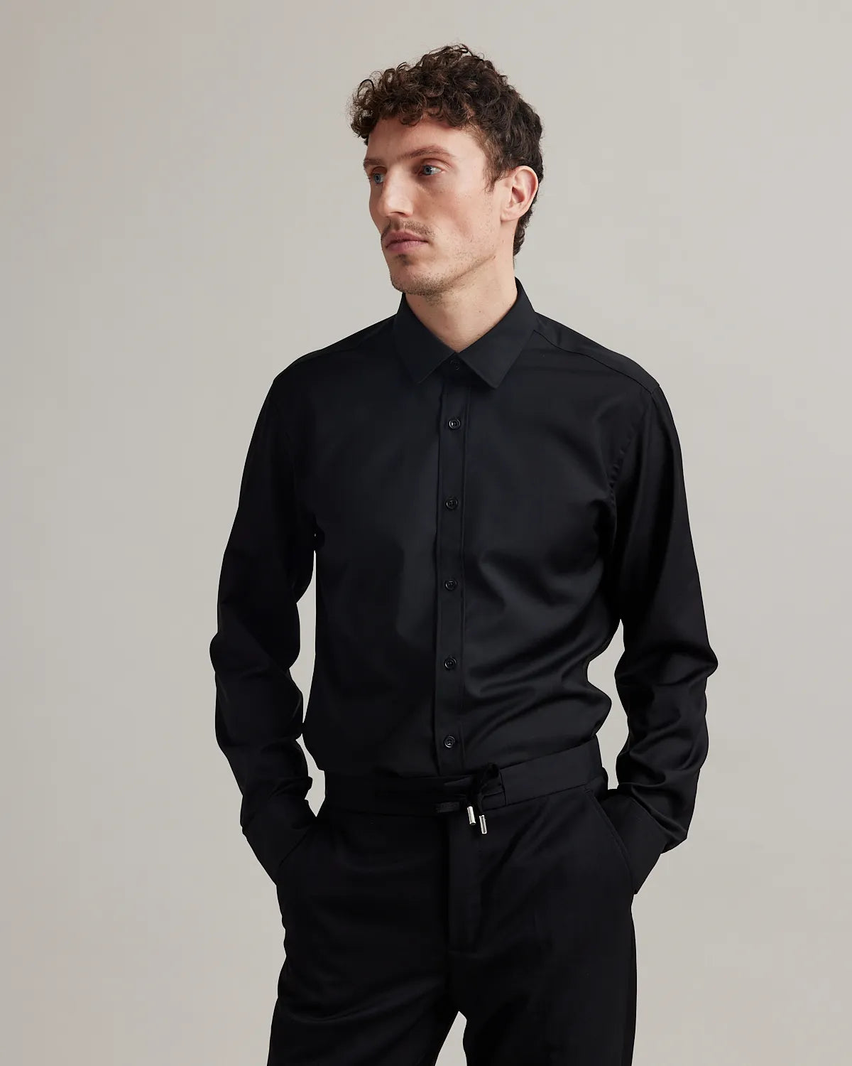 Man wearing a black slim fit merinowool dress shirt and black pants on a plain background