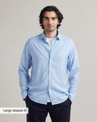 Man wearing a light blue merino shirt and white t-shirt on Navy trousers with a plain background