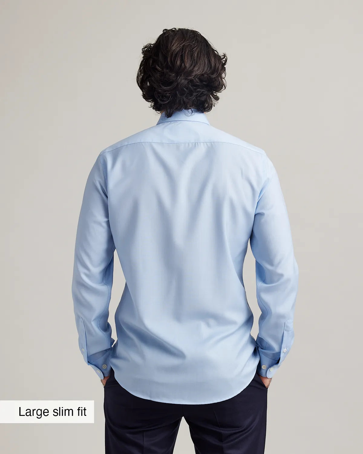 Man wearing a light blue dress shirt from behind on a plain background