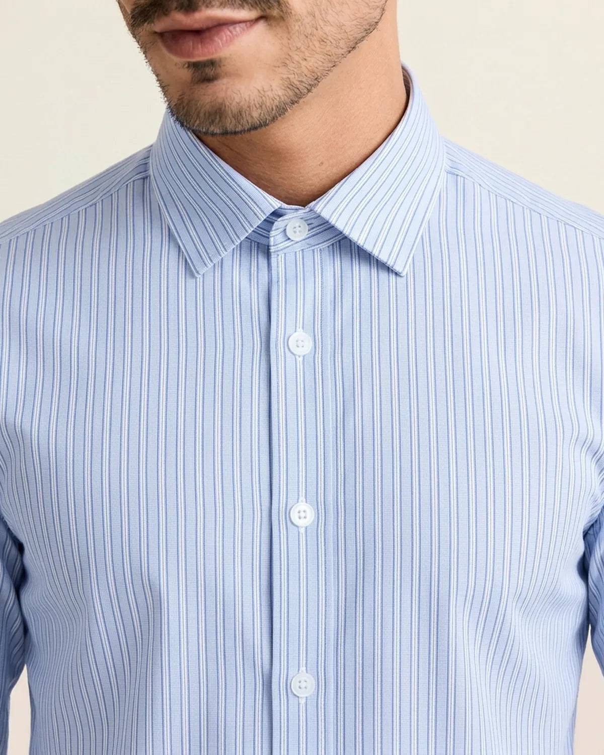 Close-up of a person wearing a light blue striped shirt featuring the collar and buttons with a beige background