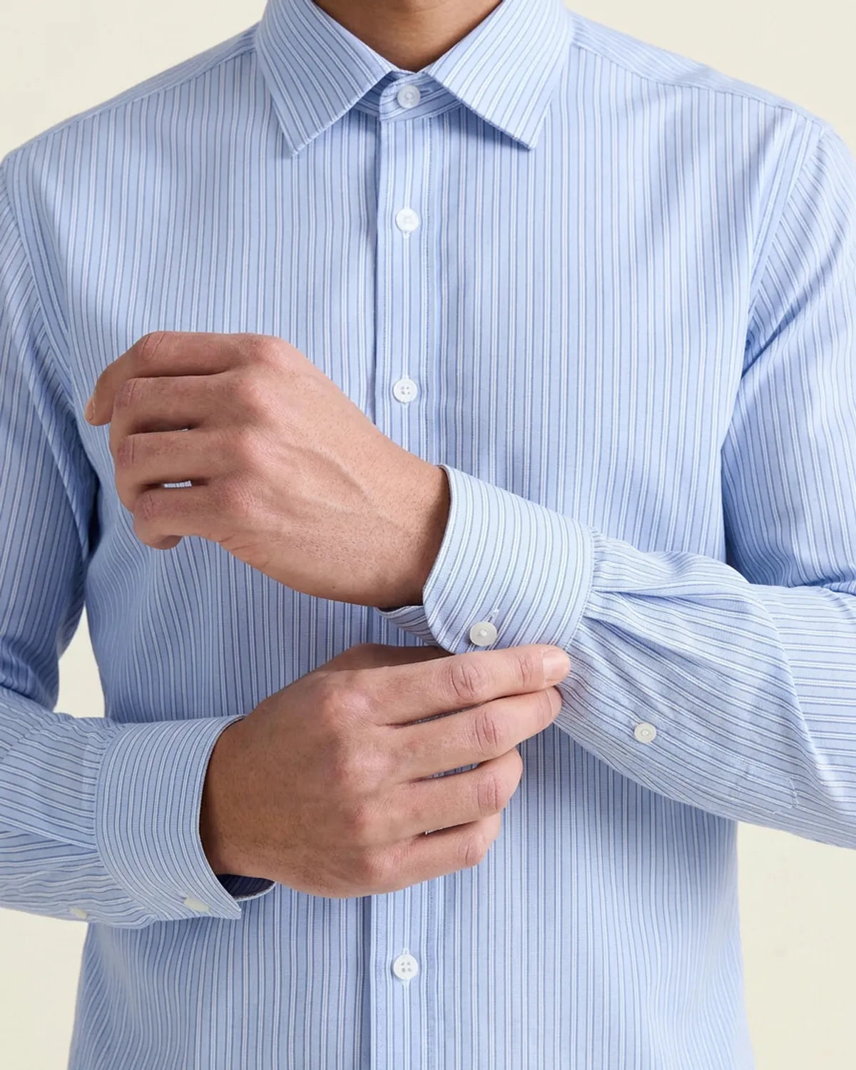 man adjusting the cuffs on a light blue striped merinowool shirt 