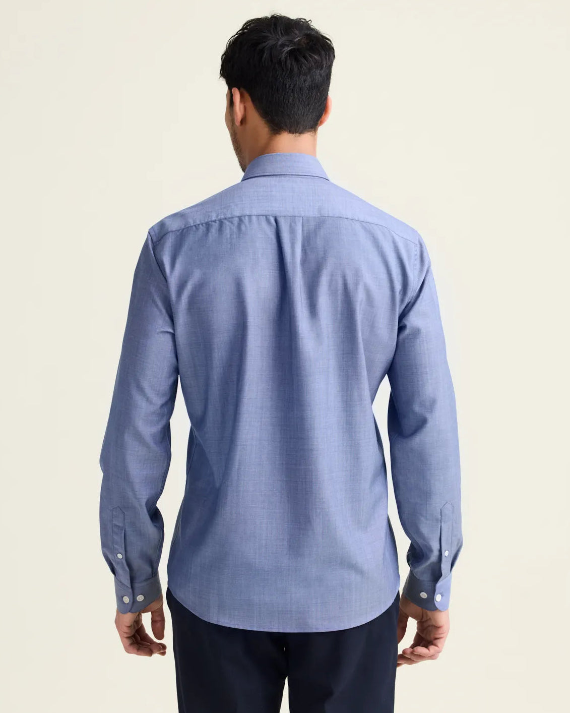 Backview of man wearing a light blue denim merino wool shirt from Wolk with long sleeves untucked on a navy pants