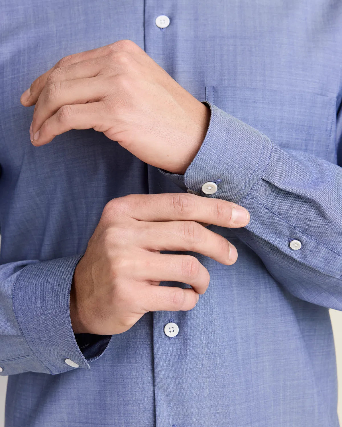 Close-up of a person wearing a light blue denim merino shirt with buttons being adjusted.
