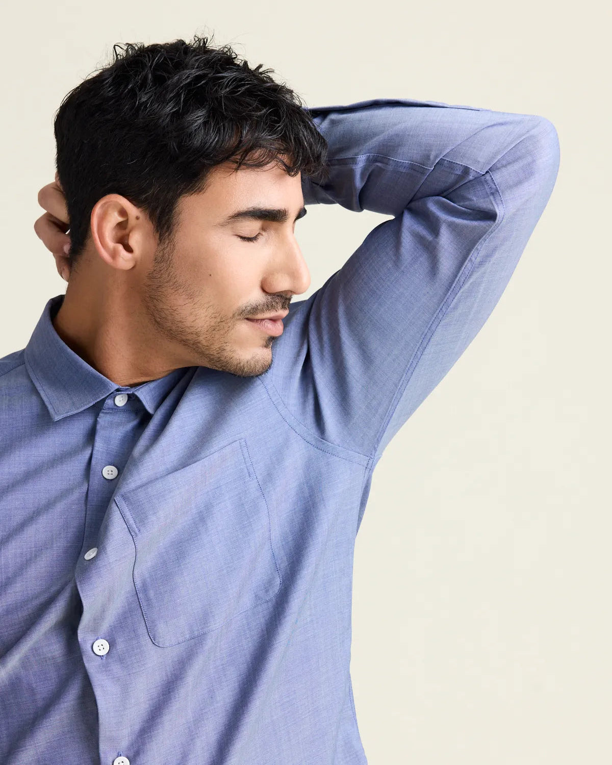Man smells his armpit wearing a merino dress shirt in light blue denim color with chest pocket.