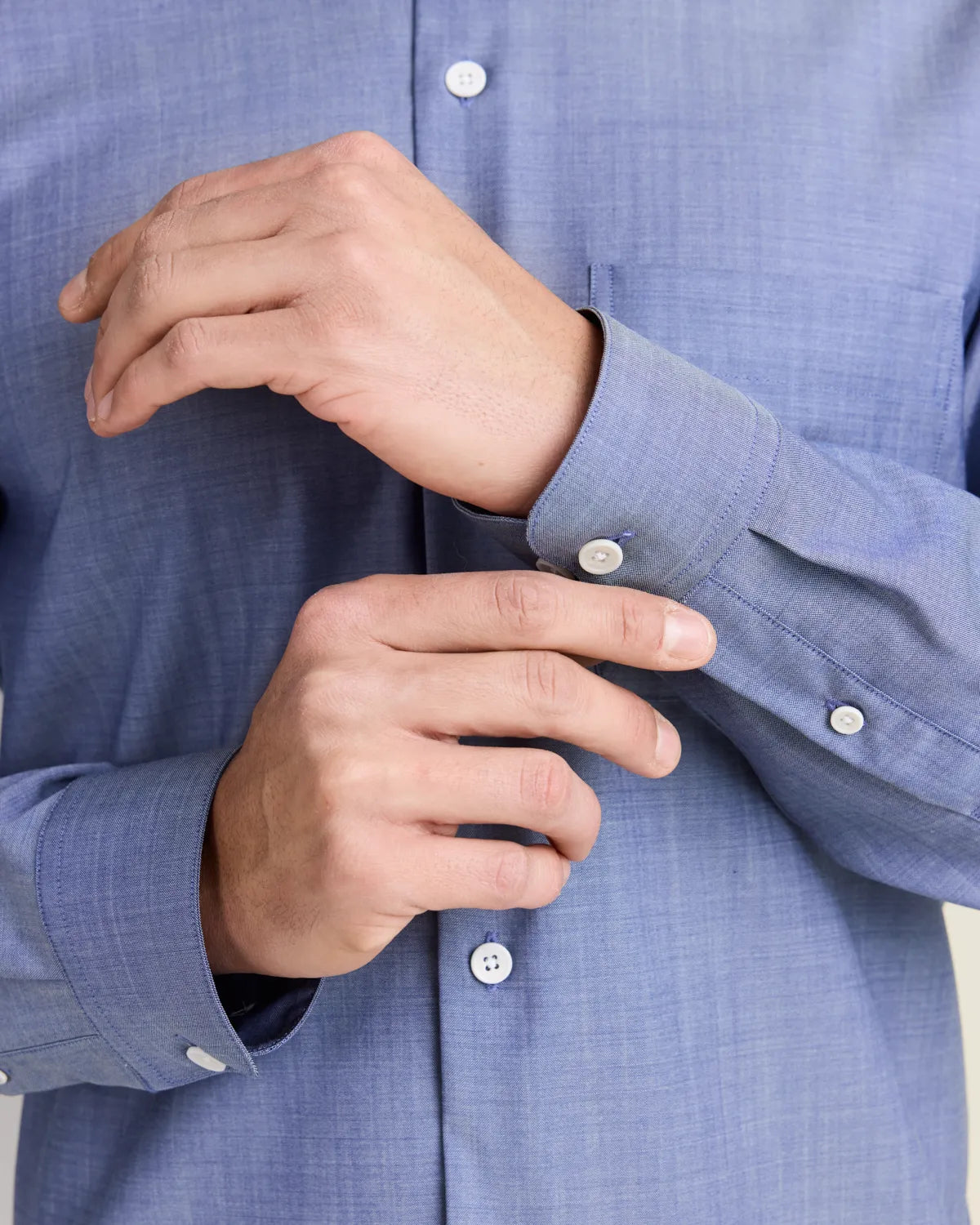 close up of a man adjusting the cuffs of a light blue denim merino shirt 