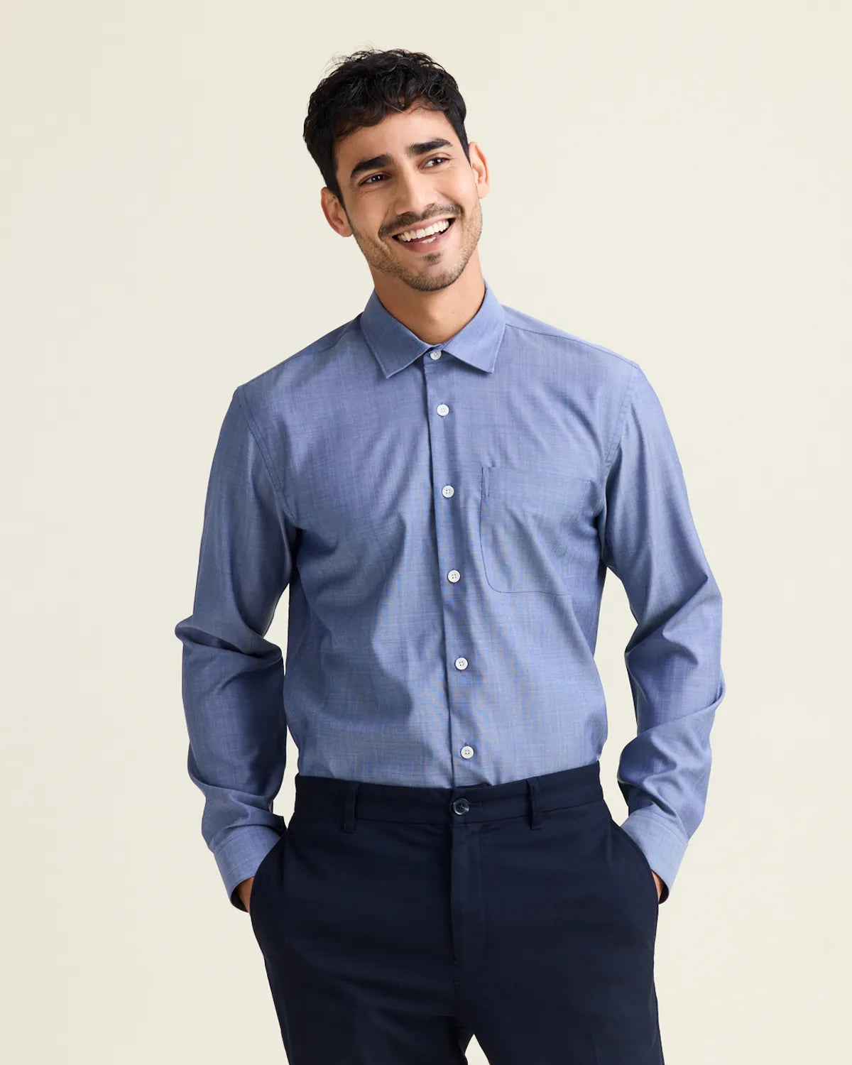 Man wearing a light blue denim merinowool dress shirt from the brand Wolk and dark pants against a beige background