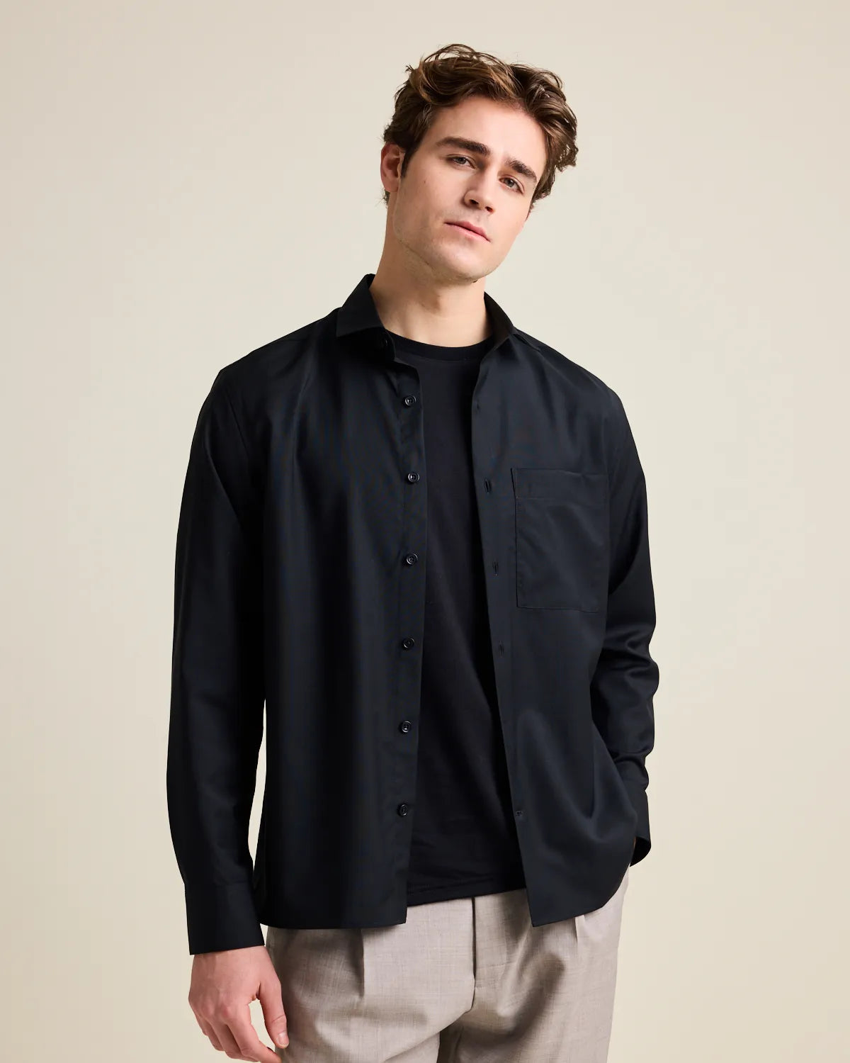 Man wearing a black merino wool  button-up shirt from Wolk over a black t-shirt on a beige background