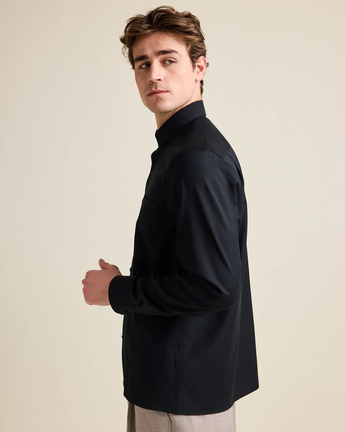 Side view of a man wearing a black merino shirt against a beige background