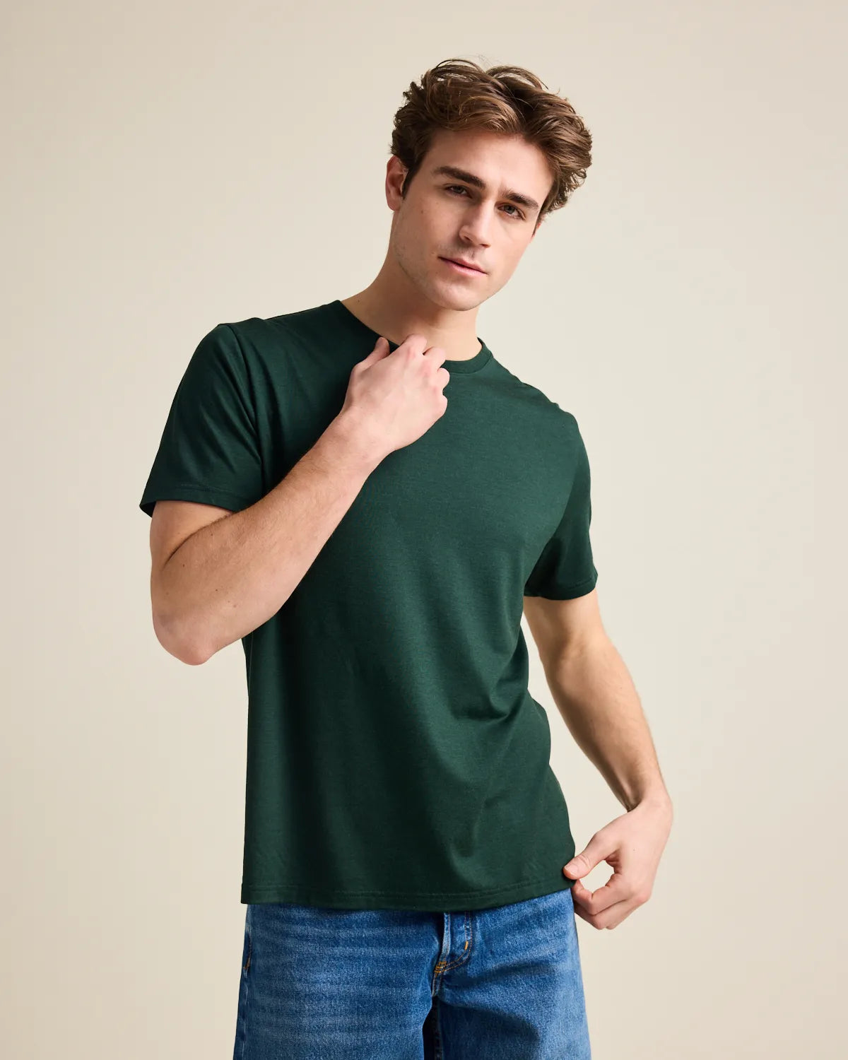 Man wearing a dark green merinwool t-shirt on blue jeans against a beige background