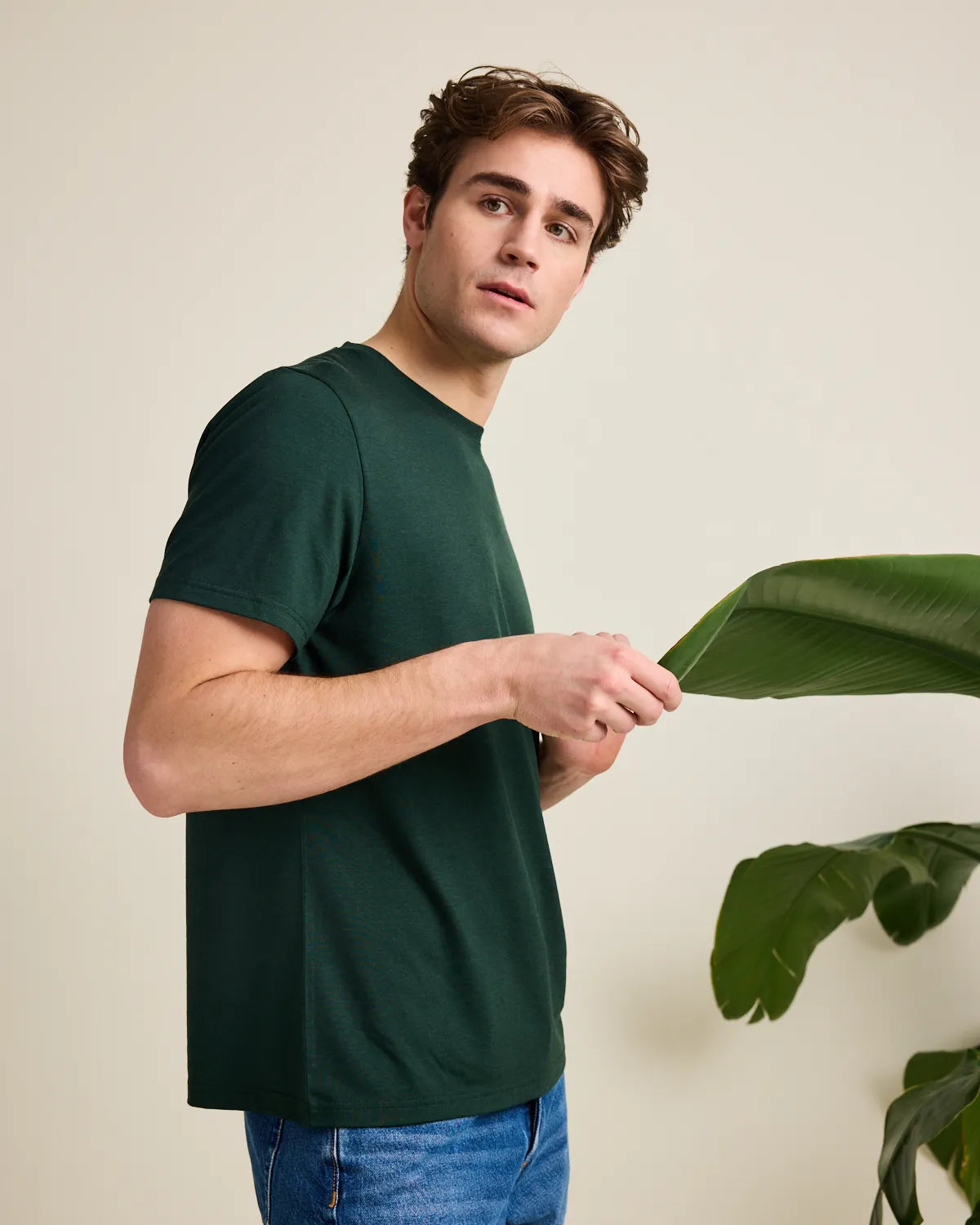 Man wearing a green t-shirt holding a plant leaf against a beige background