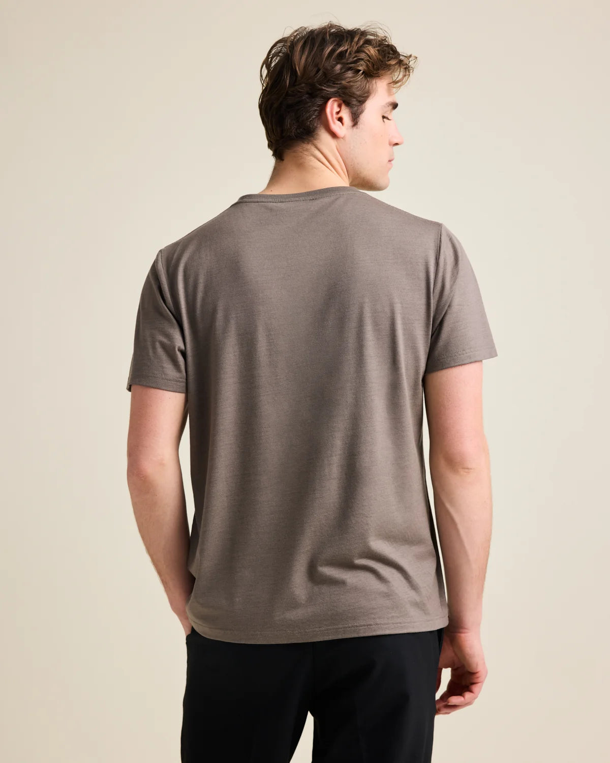 Back view of a man wearing a brown merino t-shirt against a beige background