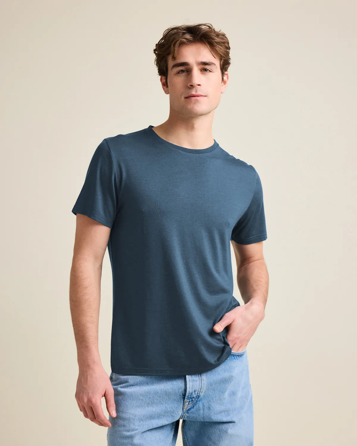 Man wearing a denim-blue merino t-shirt from Wolk and jeans against a beige background