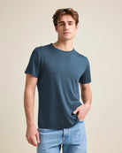 Man wearing a denim-blue merino t-shirt from Wolk and jeans against a beige background